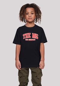 Black t-shirt featuring bold red text "THE MG CAR COMPANY" in a distressed style. Paired with olive green cargo pants.