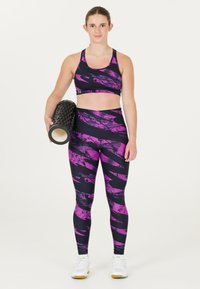 Svart sportbh och leggings med rosa abstrakta mönster, med hög midja. Modellen håller en strukturerad svart skumrulle.