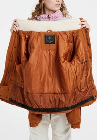 Bruine corduroy jas met een zachte crème fleece kraag. De binnenvoering is glad en oranje, met zakken en een merklabel.