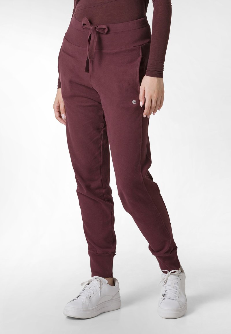 Bordeauxrode joggingsbroek met een hoge tailleband, trekkoord en zijzakken. Tapered pijp met geribbelde boorden. Gecombineerd met witte sneakers.