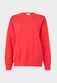 Sudadera roja hecha de un tejido suave, con un escote redondo, mangas largas y un pequeño logo en el pecho. Textura lisa con puños acanalados.