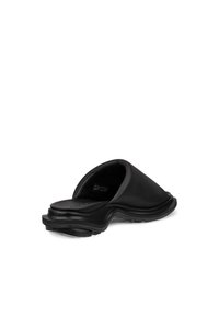 Chaussure noire à enfiler avec un design moulé, présentant un matériau supérieur lisse et une semelle texturée. Silhouette minimaliste et courbée.