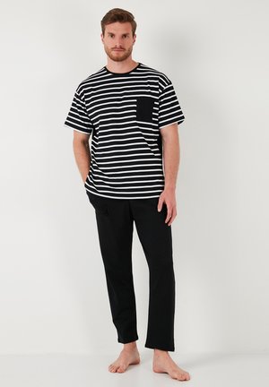 Sorte og hvide stribede T-shirt med korte ærmer og brystlomme, parret med sorte, lige ben bukser. Glat stof, afslappet pasform, minimalistisk design.