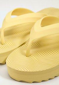Tongs jaunes à plateforme avec semelles texturées à motif ondulé et larges brides d'orteil, présentées en vue rapprochée et en angle.