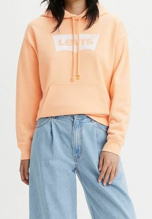 Peach hooded sweatshirt with a white Levi's logo, featuring a front pocket and drawstrings. Paired with loose blue denim jeans.
