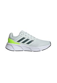 Botte de sport gris clair avec tige en maille, trois rayures gris foncé, accent vert fluo au niveau du talon, semelle intercalaire blanche et semelle extérieure noire.