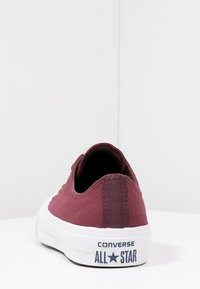 Bordowy niski tenisówka Converse All Star z białą podeszwą, widziana od tyłu na białym tle.