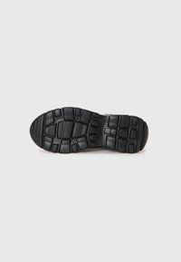 Black athletic shoe sole with a textured, patterned rubber surface. Features a sturdy design with deep grooves and rounded toe.