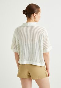 Kortärmad, vit stickad topp med öppen väv och polokrage, matchad med bruna shorts. Strukturerat tyg och avslappnad passform.