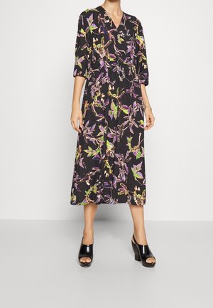 Czarna sukienka midi z fioletowo-zielonymi kwiatowymi wzorami, dekoltem w kształcie litery V, rękawami do łokcia i czarnymi butami na słupku z odkrytymi palcami.