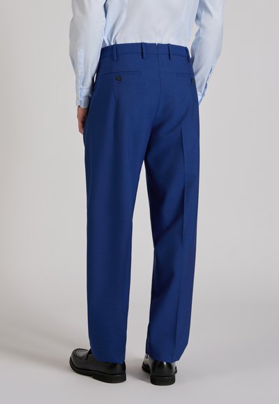 Man wearing tailored royal blue trousers, light blue shirt, and black dress shoes, shown from the back against a plain background.