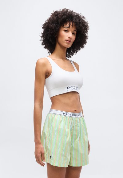 Γυναίκα με σγουρά μαλλιά που φοράει λευκό κοντό τοπ και πράσινα ριγέ μποξεράκια με λογότυπο του Polo Ralph Lauren.