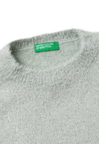 Svetle šedý, texturovaný svetr s nadýchaným vzhledem. Má kulatý výstřih a zelenou nálepku s nápisem "UNITED COLORS OF BENETTON."