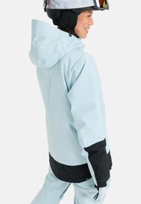 Jasnoniebieska wodoodporna kurtka narciarska z czarnym pasem i mankietami, z kapturem i kieszeniami zapinanymi na zamek. Teksturowane akcenty na rękawach.
