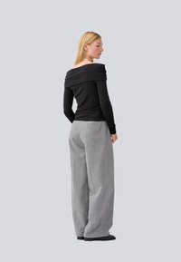 Top nero scollato con dettagli arricciati abbinato a pantaloni grigi a gamba larga con una sottile fantasia e tasche. Scarpe basse nere.