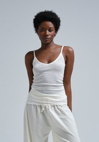 White fitted tank top with thin straps, featuring a soft, lightweight fabric. Paired with loose, white, elastic-waist pants with a ruffled detail.