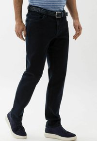 Jeans in denim blu scuro con taglio dritto, dotati di una cintura intrecciata. Abbinati a una camicia a righe blu e bianche e sneakers blu navy.