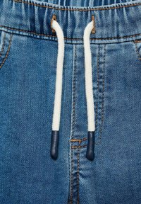 Džíny mají úzký pas s elastickým provázkem, bílými šnůrkami zakončenými tmavě modrými konci a kontrastním oranžovým prošíváním.