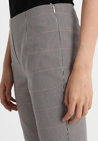 Czarno-białe spodenki w kratę z subtelnymi czerwonymi akcentami; posiadają zamek błyskawiczny i dopasowany krój. Gładka tekstura, lekką tkanina.