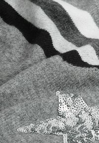 Tissu gris tricoté avec des rayures noires et blanches et une étoile en sequins argentés en embellissement en bas à droite.