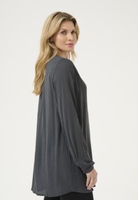 Blusa grigia a maniche lunghe realizzata in tessuto testurizzato, con una vestibilità rilassata, dettagli con polsini abbottonati e orlo arrotondato.