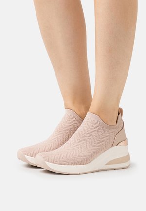 Lyserøde slip-on strikkede sneakers med chevronmønster, tykke hvide såler og trækstropper, båret på bare fødder.