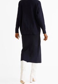 Granatowy sweter o luźnym kroju, w połączeniu z dopasowaną spódnicą do kolan. Całość dopełniają off-white kozaki do kolan.