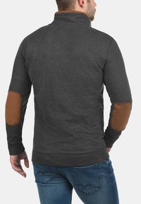 Gray pullover with a high collar, made of soft fabric, featuring brown elbow patches and ribbed cuffs. The back is smooth without embellishments.