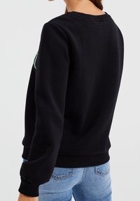 Svart sweatshirt med rund halsringning och ribbad mudd. Bakdelen har en enkel design, tillverkad av mjukt tyg med en slät yta.