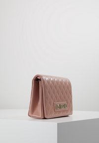 Látková růžová taška z umělé kůže s zlatým kováním, obdélníkového tvaru a klopou, s logem na přední straně.