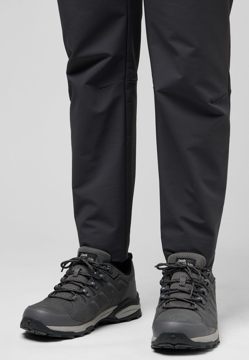 Graue Wanderschuhe mit strukturiertem Stoff, Schnürsenkeln und Gummisohlen, kombiniert mit schwarzen, schmal geschnittenen Hosen mit glatter Oberfläche und Nähten.