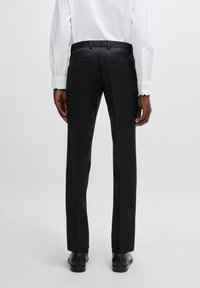 Black tailored pants with a smooth texture, featuring side and back pockets, paired with a white long-sleeve shirt.