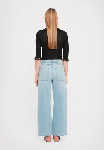 Black cropped sweater with fringe hem, paired with light blue wide-leg jeans. The jeans have two back pockets and a straight cut.