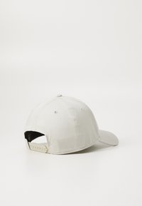 Állítható baseballsapka világoskrém színű anyagból. Gömbölyű karimával, varrott részletekkel és műanyag pántos záródással a hátsó részen.