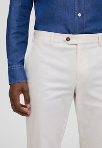 Beige broeken met een zachte textuur, voorzien van een knoopsluiting aan de voorkant en riemlussen, gecombineerd met een blauwe spijkerblouse.
