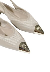 Décolleté beige con cinturino alla caviglia, punta appuntita, parte superiore in rete texturizzata e accento metallico dorato sulla punta con dettaglio decorativo del logo.