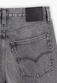 Zadní kapsa vybledlých černých džín Levi's s charakteristickým prošíváním, poutky na pás a černou koženou etiketou Levi Strauss & Co. nad pasem.