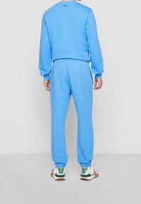 Person wearing a blue sweatshirt and matching joggers with white and green sneakers, standing facing away against a plain background.