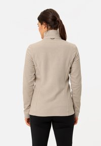 Giacca in fleece beige chiaro con collo alto, design aderente e texture liscia. Presenta un piccolo logo sulla parte posteriore del collo.