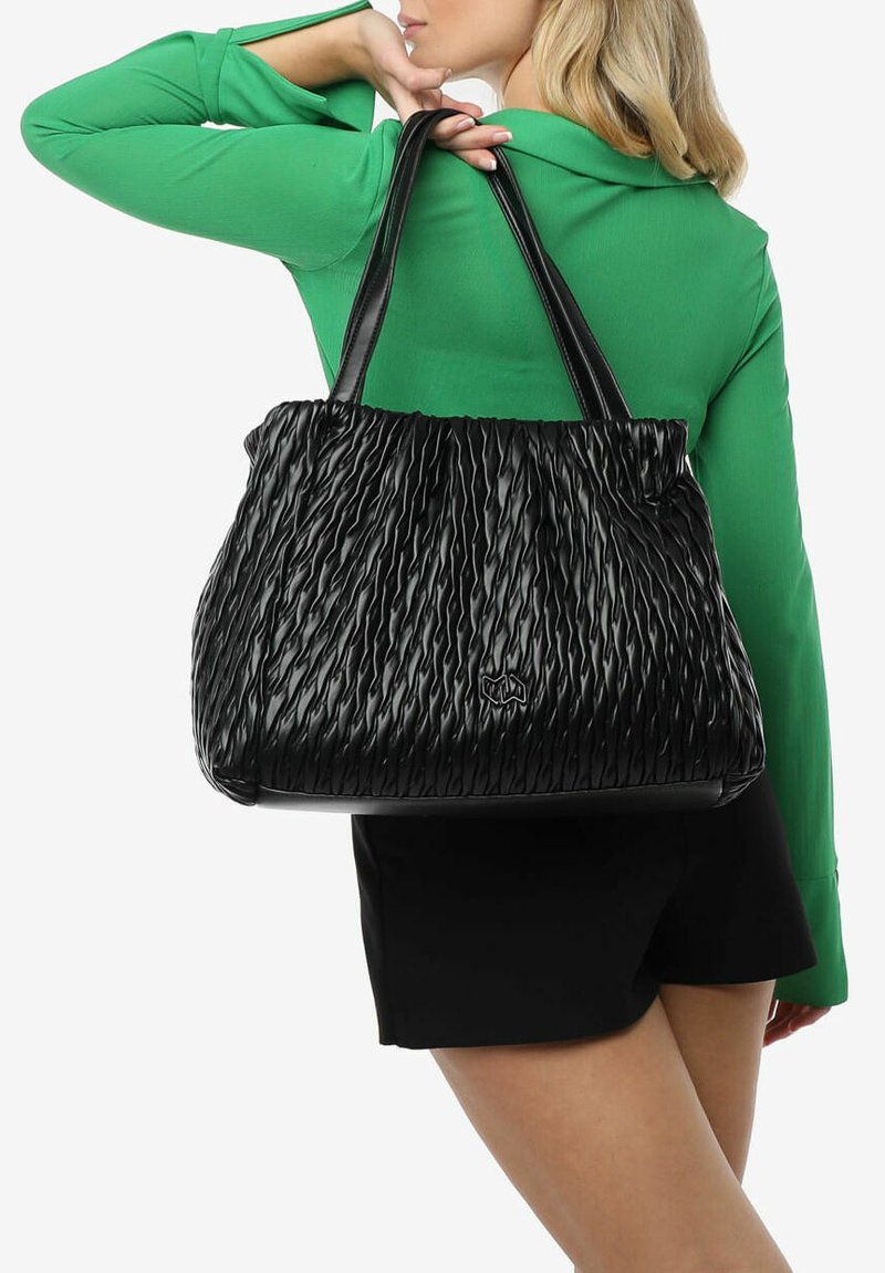 Zwarte geplooide tote bag met een gestructureerd oppervlak en gladde leren handvaten, met een reliëf logo aan de voorkant.
