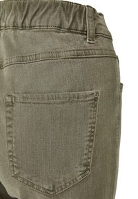Pantalones de mezclilla verde oliva con cintura elástica, con un bolsillo trasero y detalles de costura visibles. Tejido texturizado.