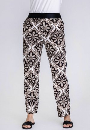 Slim-fit pants with a black, beige, and white geometric floral pattern and black elastic waistband, modeled with black open-toe sandals.