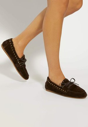 Brown suede moccasin-style shoes with gold stud accents, lace-up detail, and a flexible sole, featuring a soft inner lining.