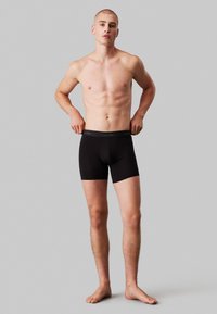 Schwarze Baumwoll-Boxershorts mit einem elastischen Bund, der das Calvin Klein-Logo zeigt, körpernahe Passform und eine weiche, glatte Textur.