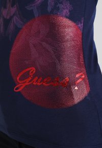 Gráfico de un círculo rojo con puntos y la palabra "¿Adivinas?" en cursiva sobre un fondo de tela azul oscuro.