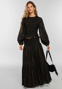 Conjunto negro de dos piezas con top smockeado y falda de volantes, con rayas metálicas doradas, mangas largas abullonadas y falda con volantes peplum.