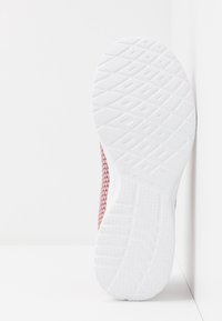 Röd och vit idrottssko med en texturerad vit gummisula med triangulära mönster och en mesh-överkonstruktion för andningsförmåga.