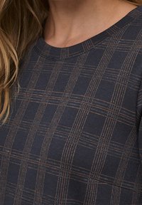 Maglia blu navy con un motivo a griglia e linee arancioni, colletto tondo e tessuto strutturato. La vista ravvicinata evidenzia i dettagli del design.