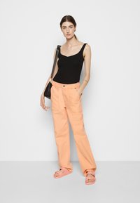 Top preto sem mangas combinado com calças largas pêssego com bolsos frontais. Sandálias rosa claro completam o look.