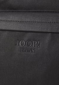 Črno blago z gladko teksturo prikazuje izbočen logo "JOOP! JEANS" na očitnem mestu. Preprost dizajn brez dodatnih vzorcev ali dodatkov.